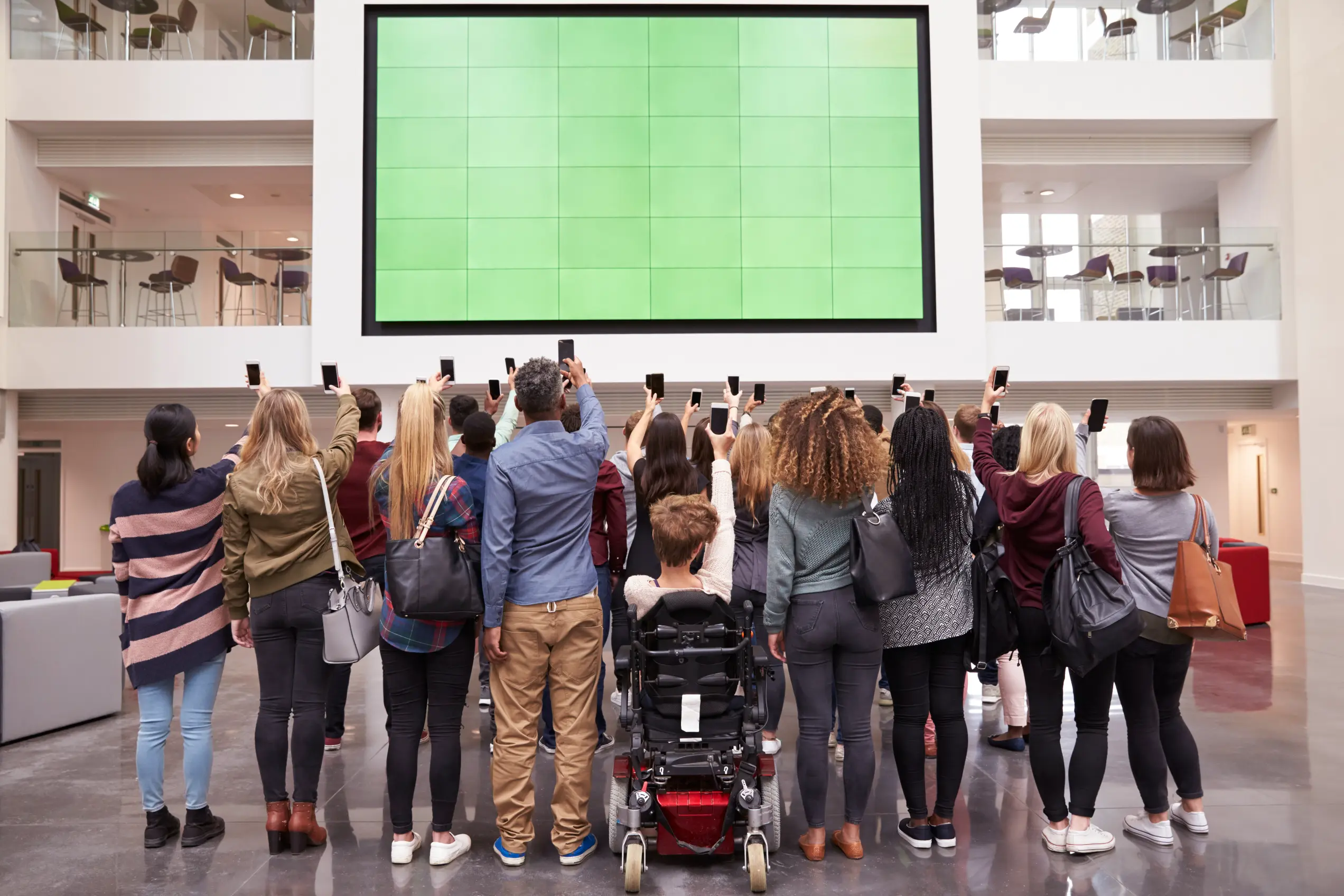Grupa studentów fotografująca telefonami duży ekran w holu uczelni